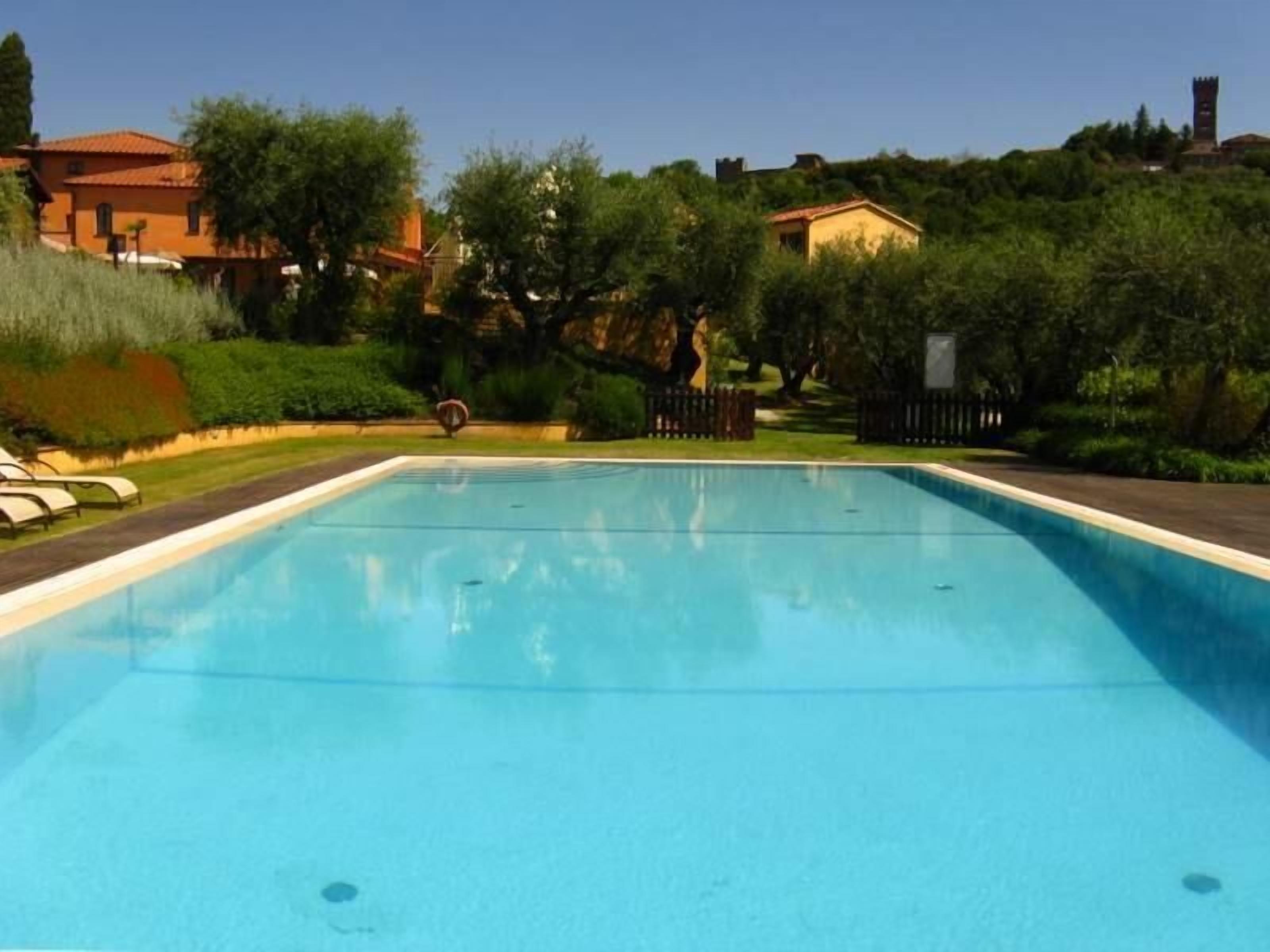 A rectangular swimming pool with clear blue water, surrounded by a well-maintained garden with various shrubs and trees.