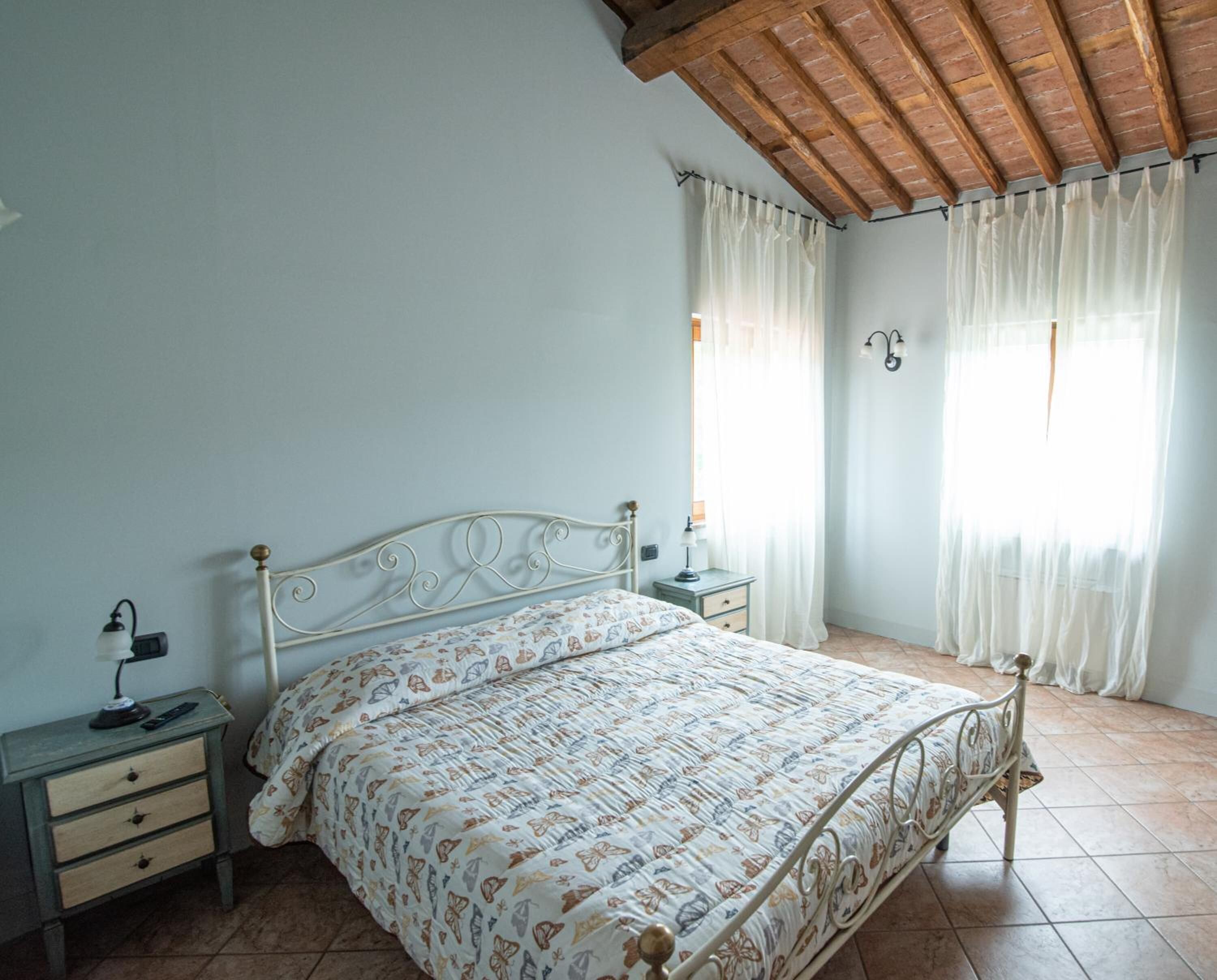 Quarto com estrutura de cama em metal, mesa de cabeceira com abajur e criado-mudo.