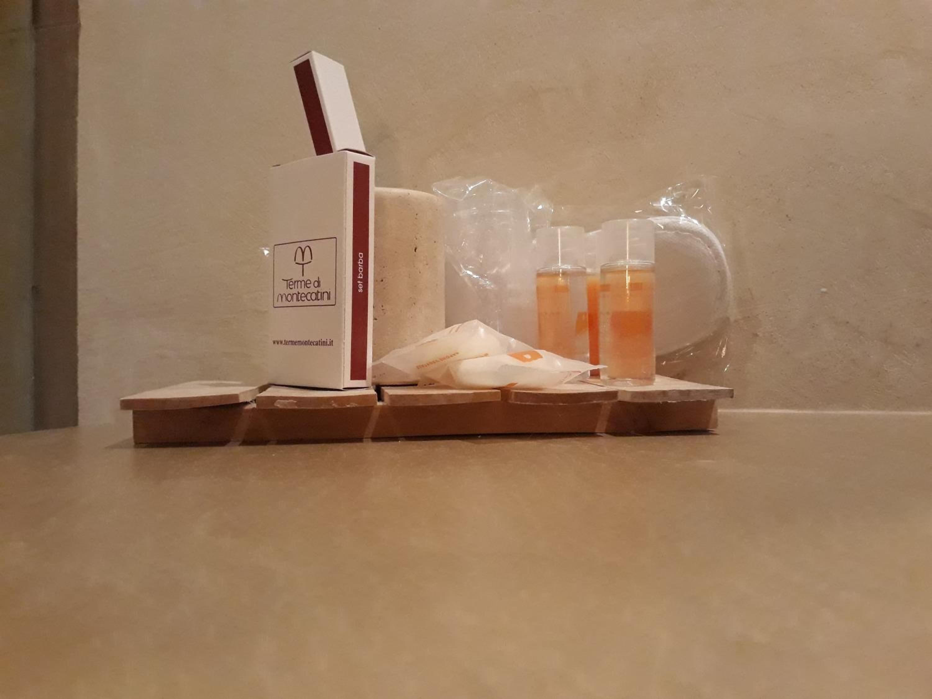 Eine Kiste mit dem Aufdruck "Termini di Montecatini", einer Internetadresse, einem Plastiksack und zwei klaren Flaschen mit orangefarbener Flüssigkeit.