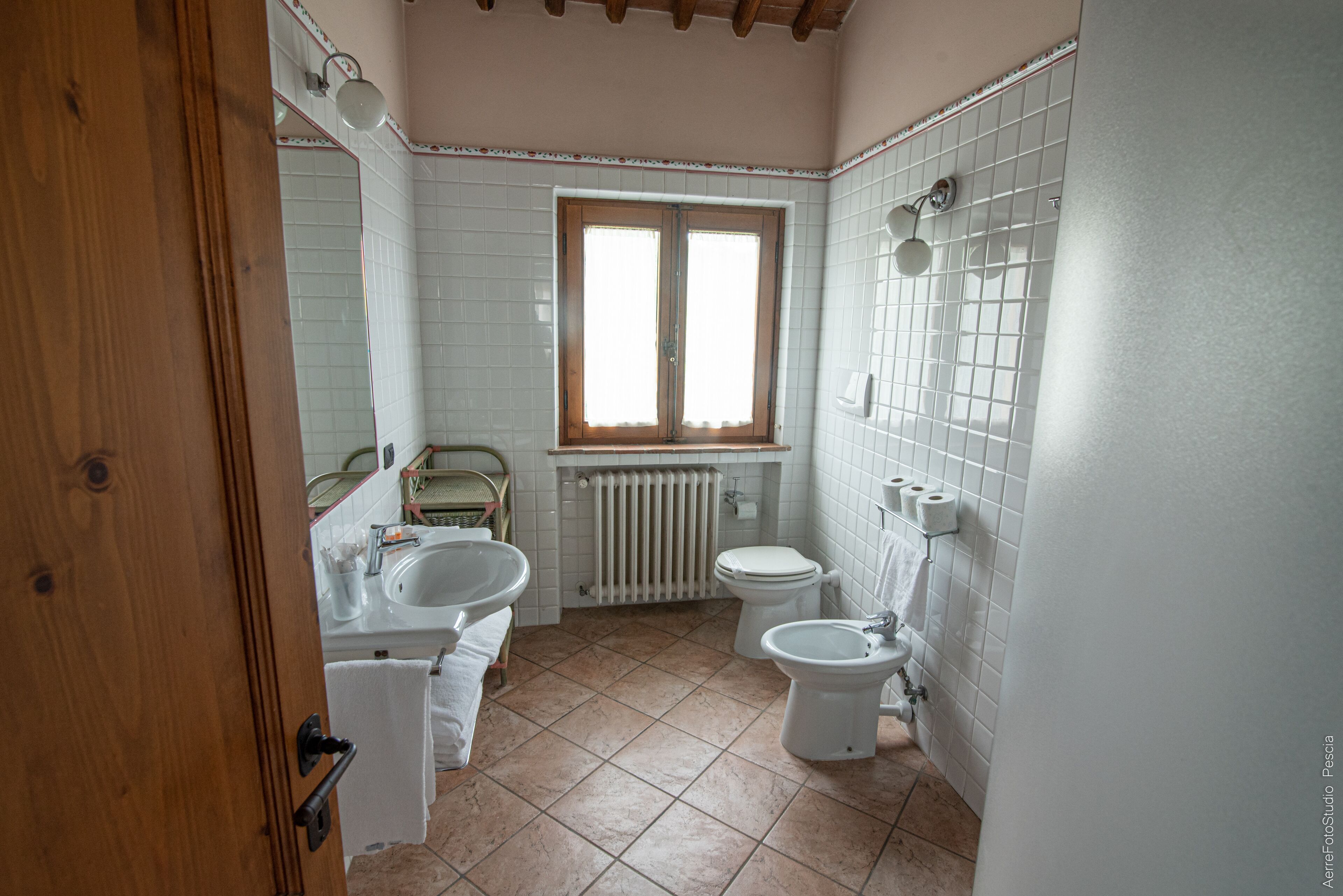 A bathroom with white tiles, a window, a radiator, a toilet, a sink, and a shower.