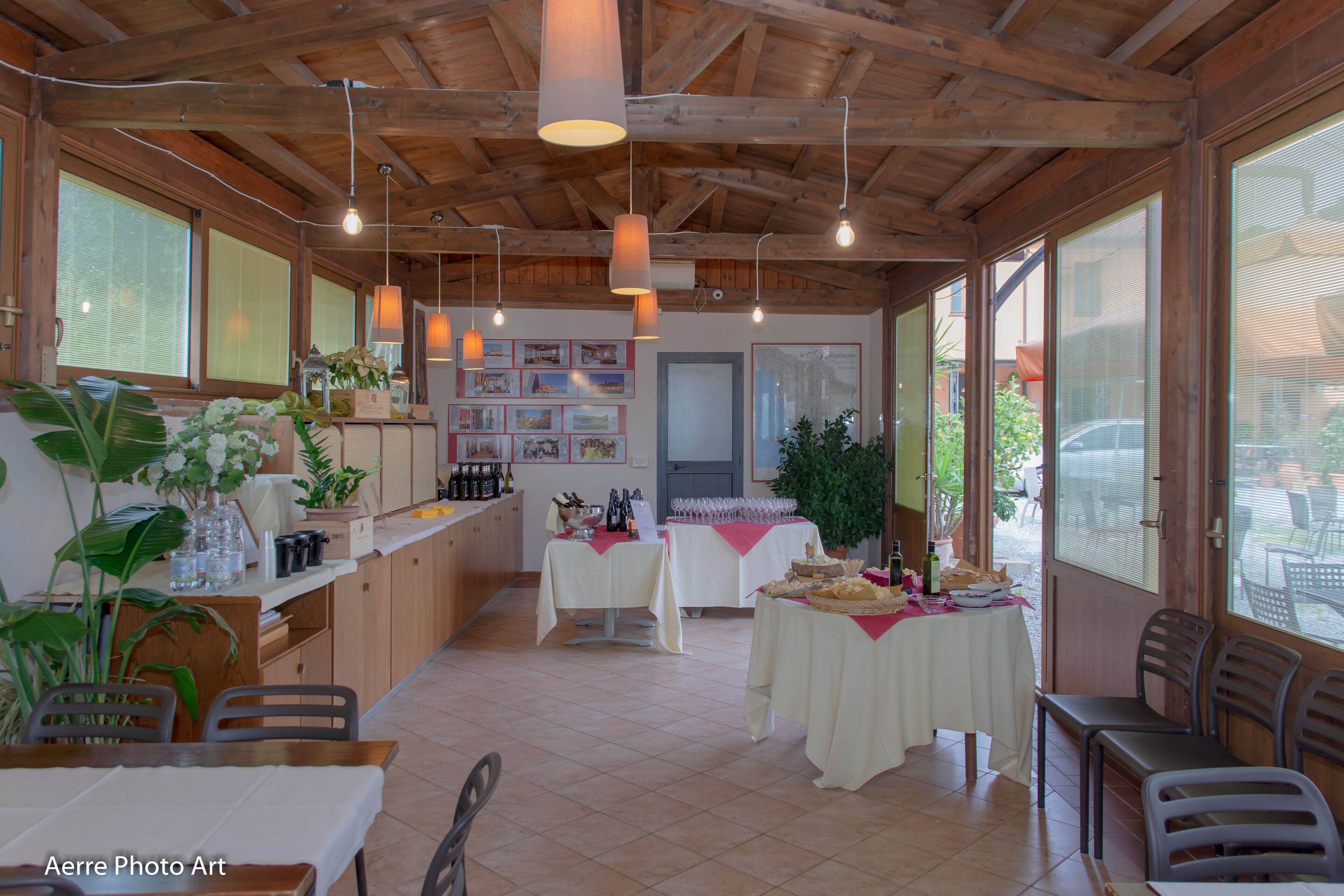 A spacious room with wooden beams, large windows, and tables set up for dining.