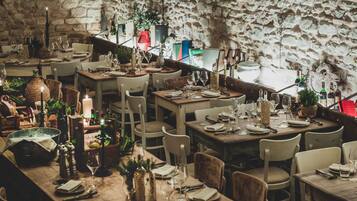 A rustic dining area with stone walls, wooden tables, and various dining utensils.