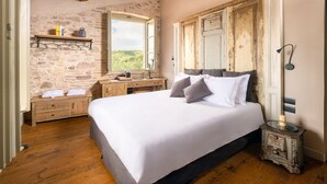 Une chambre avec un grand lit, une tête de lit en bois, un mur en pierre, un plancher en bois et une commode rustique.