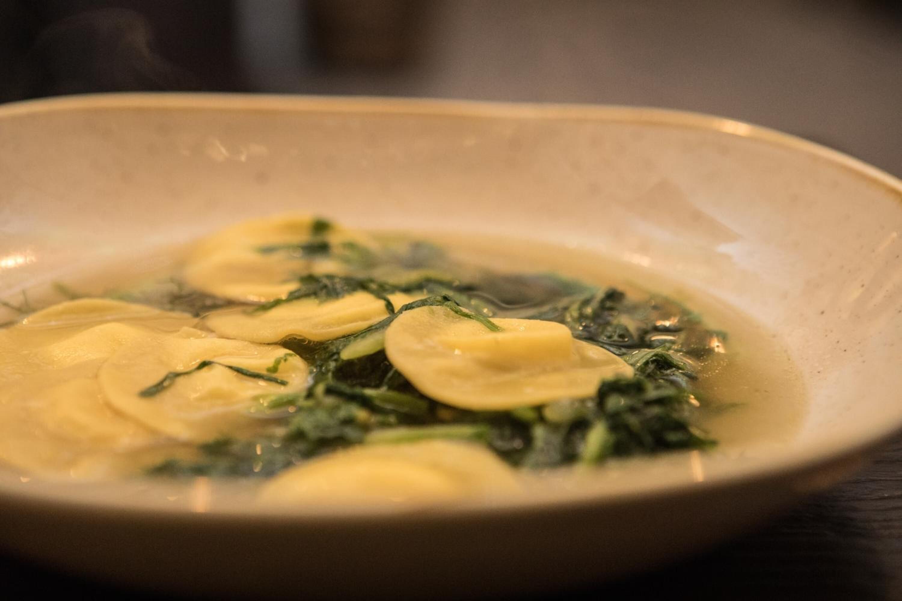 A bowl of soup with leafy greens and dumplings.