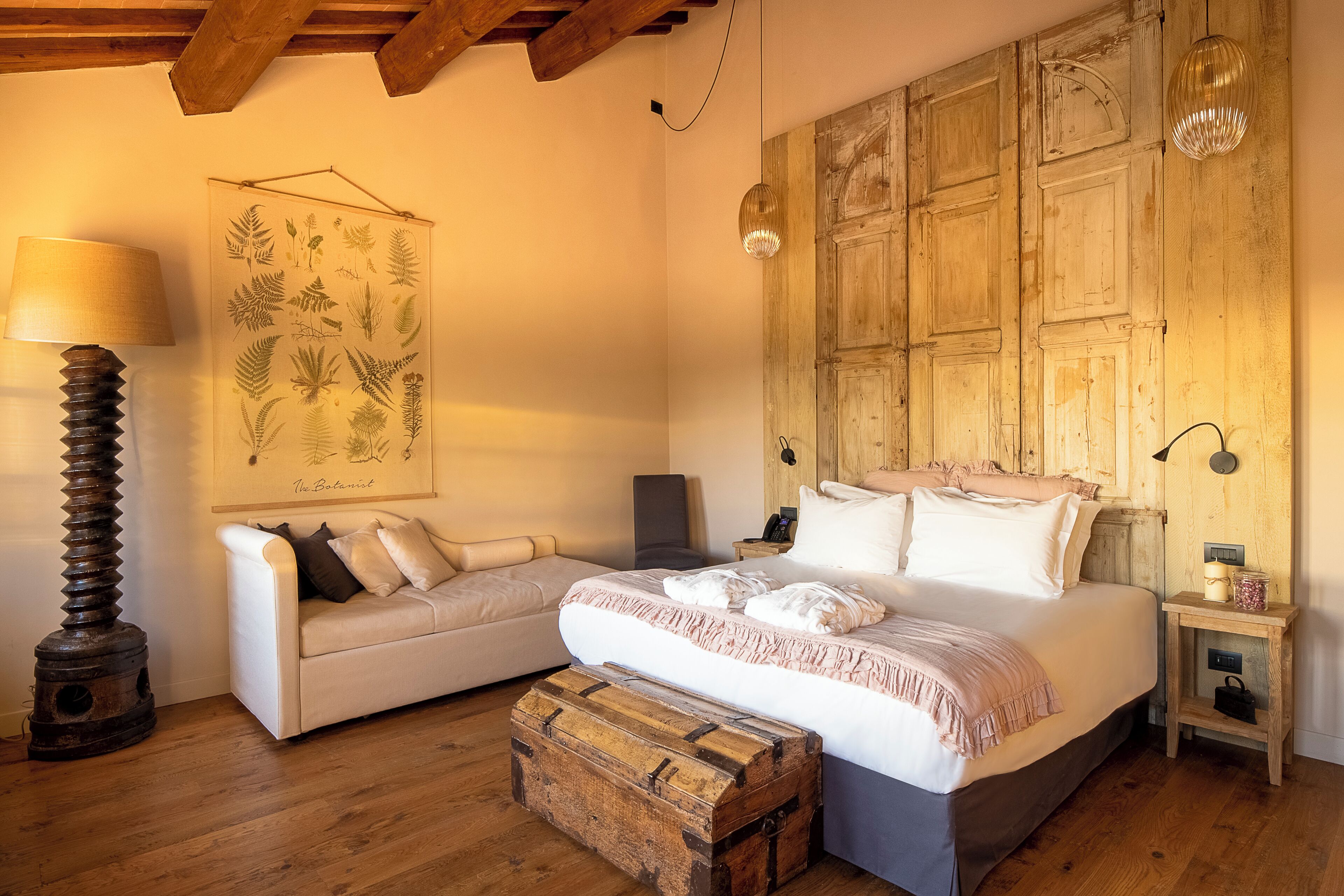 Un dormitorio acogedor con cama, sofá, un cofre de madera, una lámpara y una lámpara de pared.