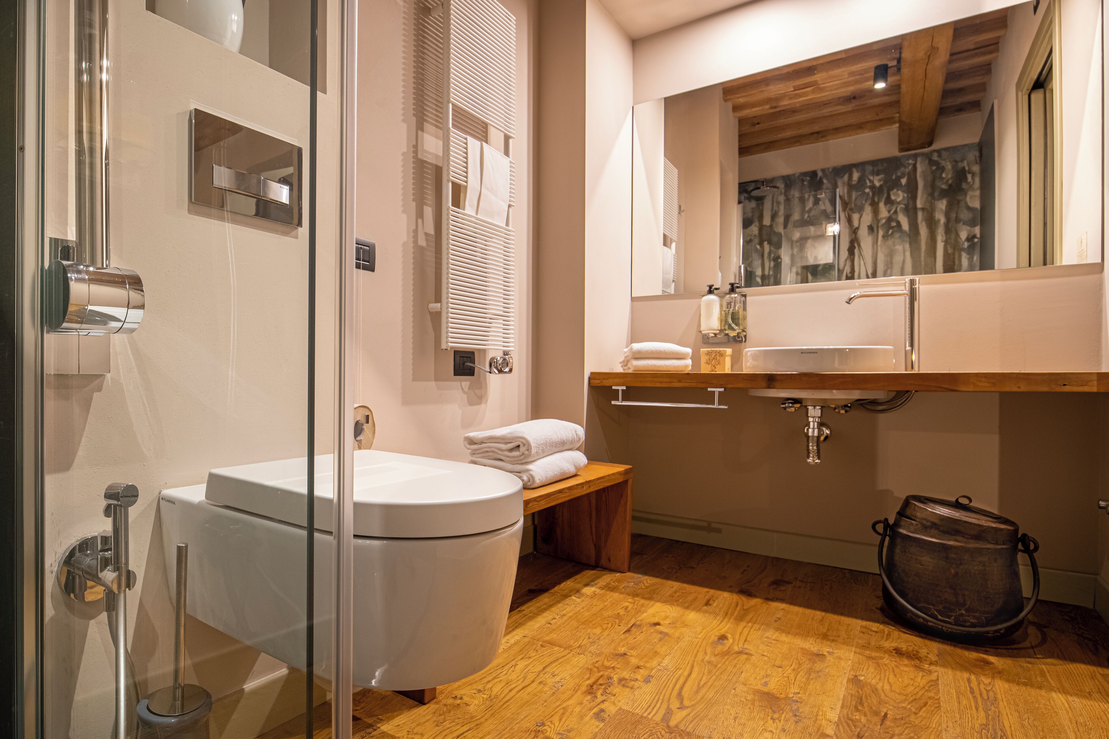A modern bathroom with a glass shower enclosure, a white toilet, a wooden bench, and a sink with a wooden countertop.