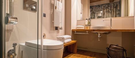 Un baño moderno con cabina de ducha de vidrio, inodoro blanco, banco de madera y lavamanos con encimera de madera.