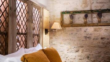 A room with a stone wall, a bed with white and mustard-colored bedding, and a wall-mounted lamp.