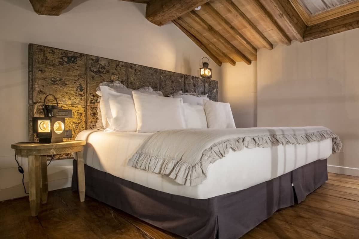 A bedroom with a large bed, wooden headboard, and a nightstand with a lantern.