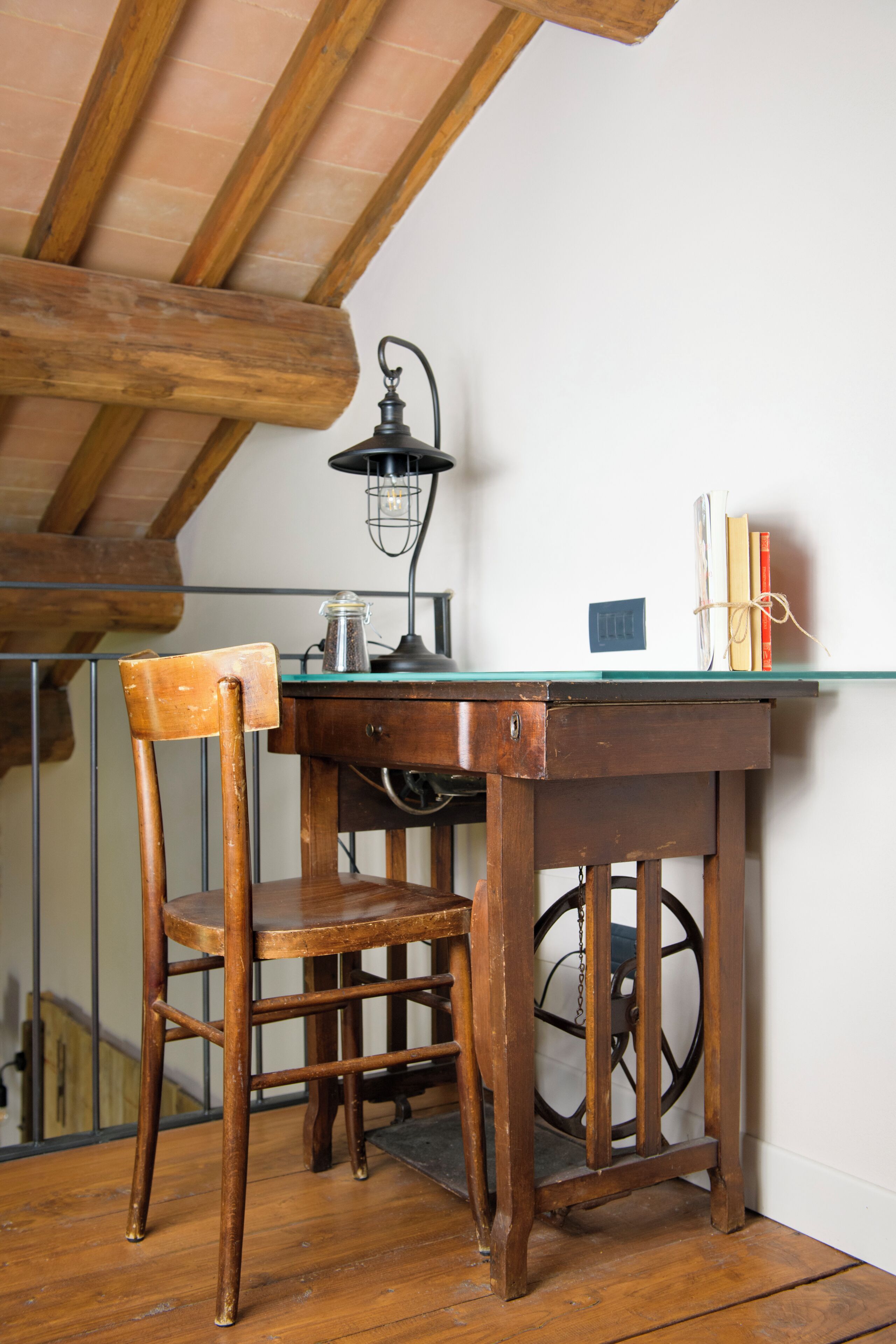 Un bureau en bois avec un plateau en verre, une lampe de style vintage et une chaise.