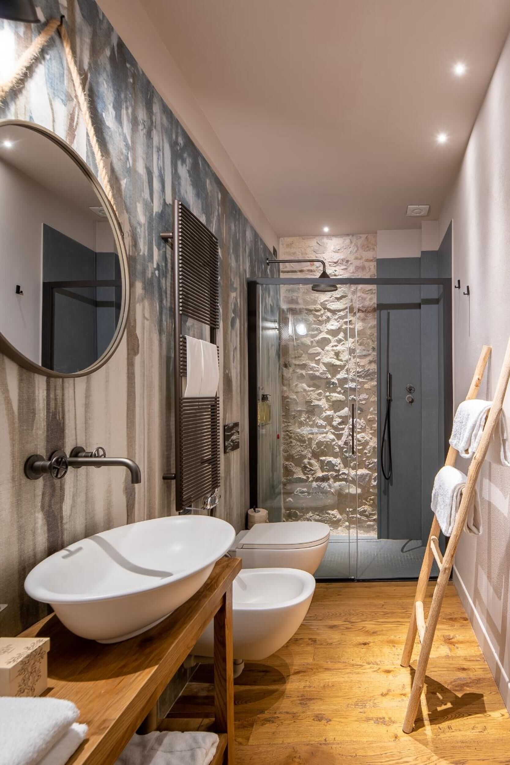 A modern bathroom with a large mirror, two sinks, a shower, and a wooden ladder.