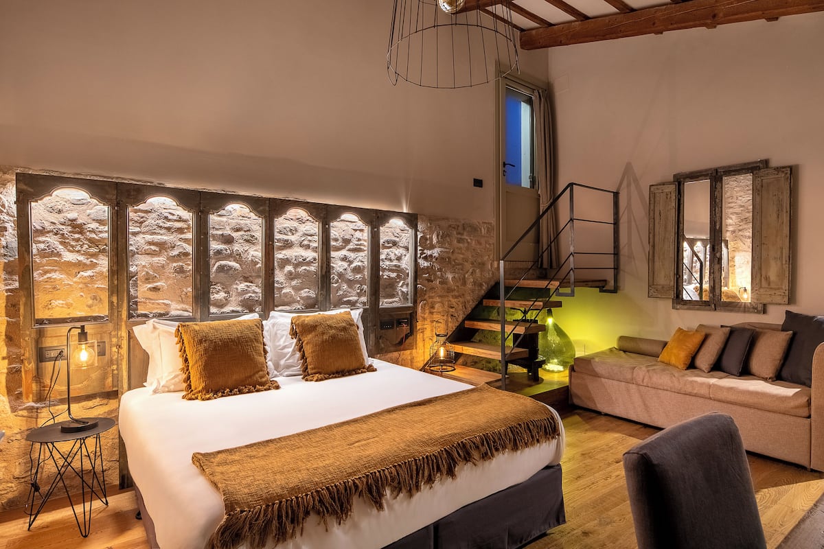 A bedroom with a large bed, a wooden staircase, and a stone wall.