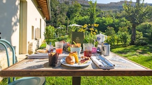 Une table dressée à l’extérieur, avec un repas composé d’un sandwich, d’une pâtisserie et de boissons, et en arrière-plan, la vue d’un bâtiment.
