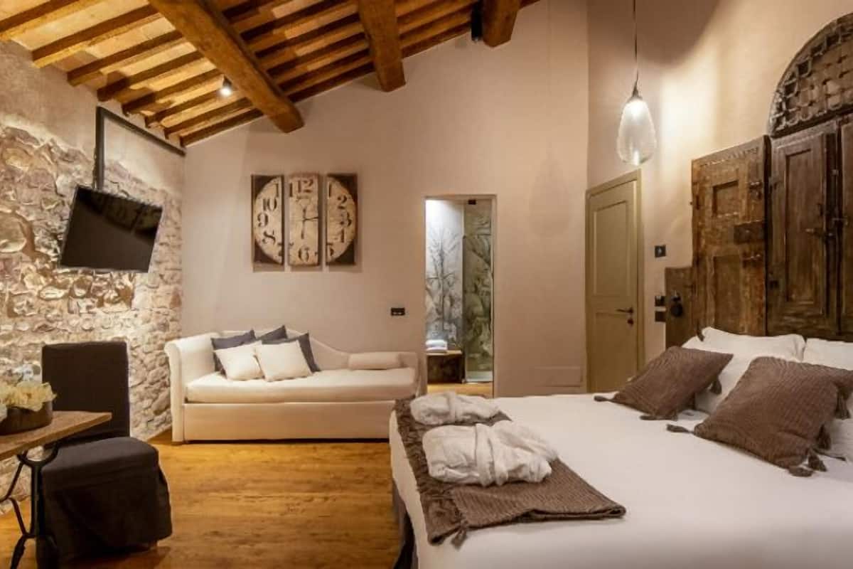 A cozy bedroom with a bed, a sofa, a wooden ceiling, and a stone wall.