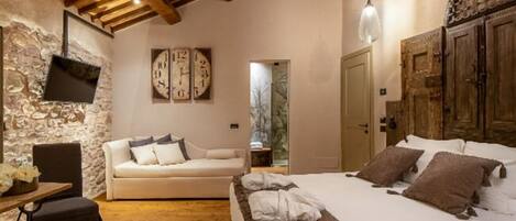 A cozy bedroom with a bed, a sofa, a wooden ceiling, and a stone wall.