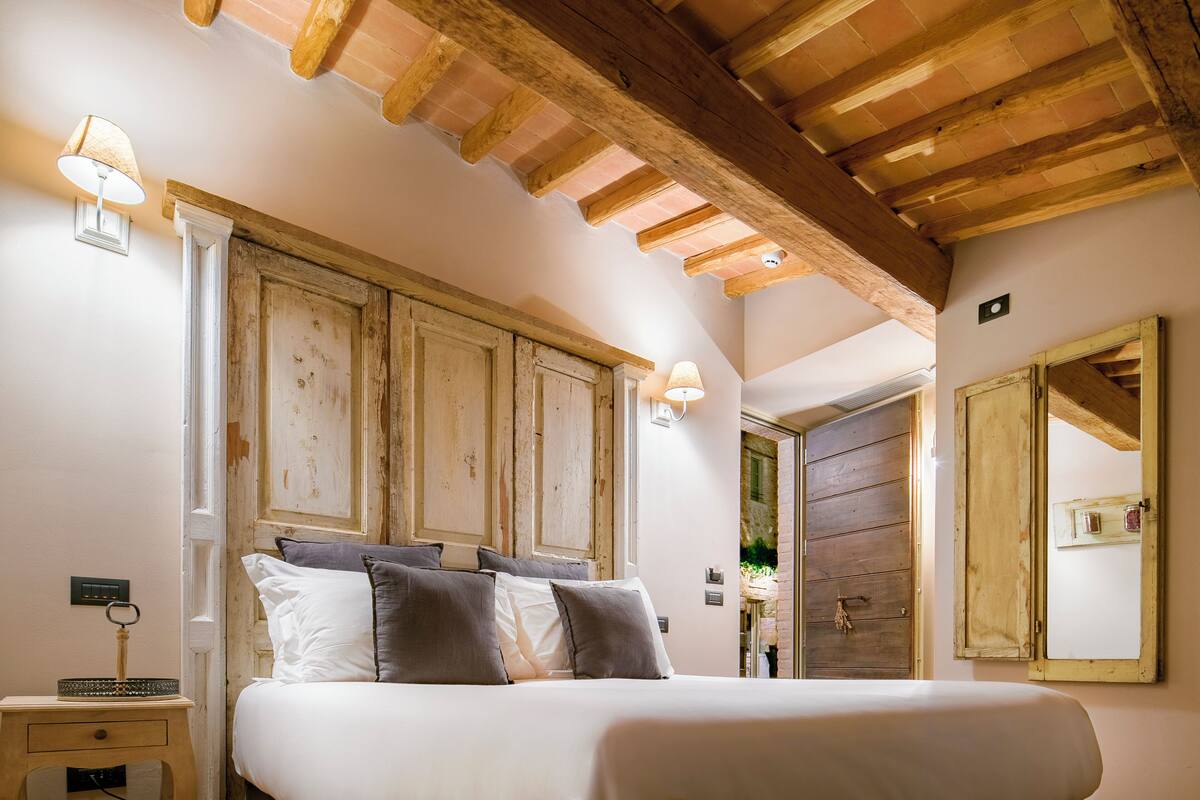 A bedroom with a large bed, wooden beams on the ceiling, and a wooden door.
