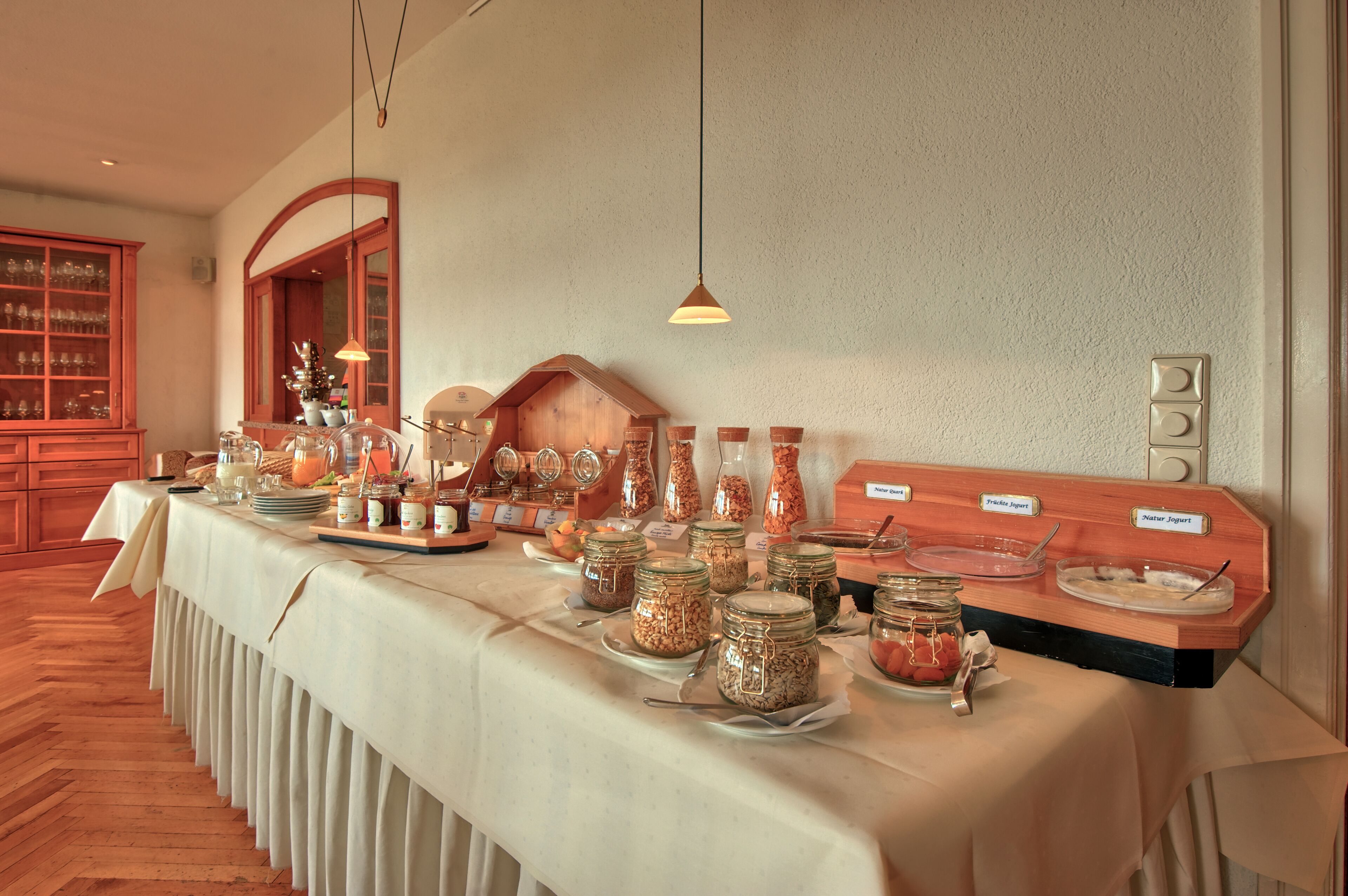 A buffet table with various food items and labels, wooden cabinets, and hanging pendant lights.
