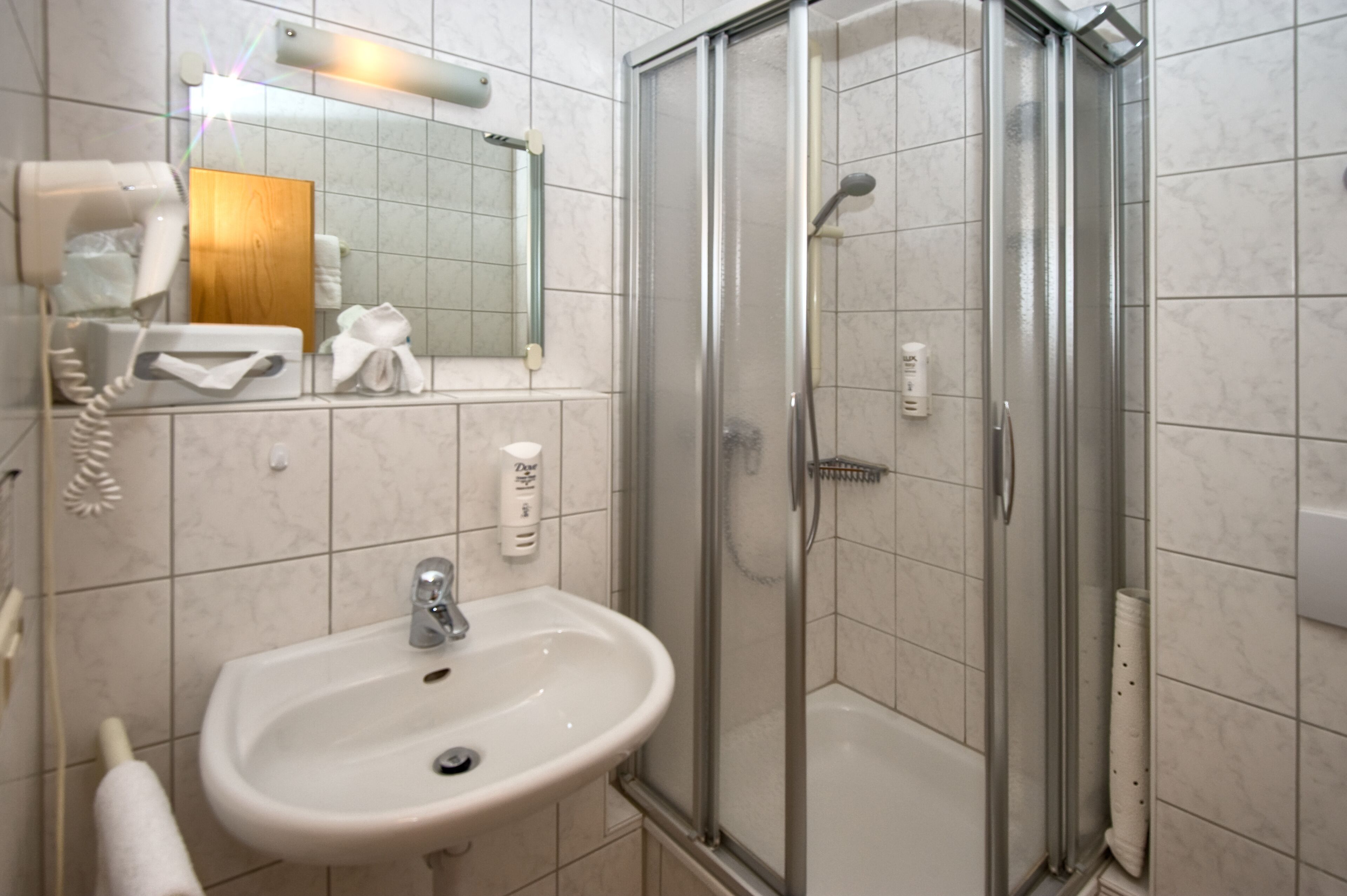 Un baño con lavamanos, espejo y ducha con mampara de vidrio.