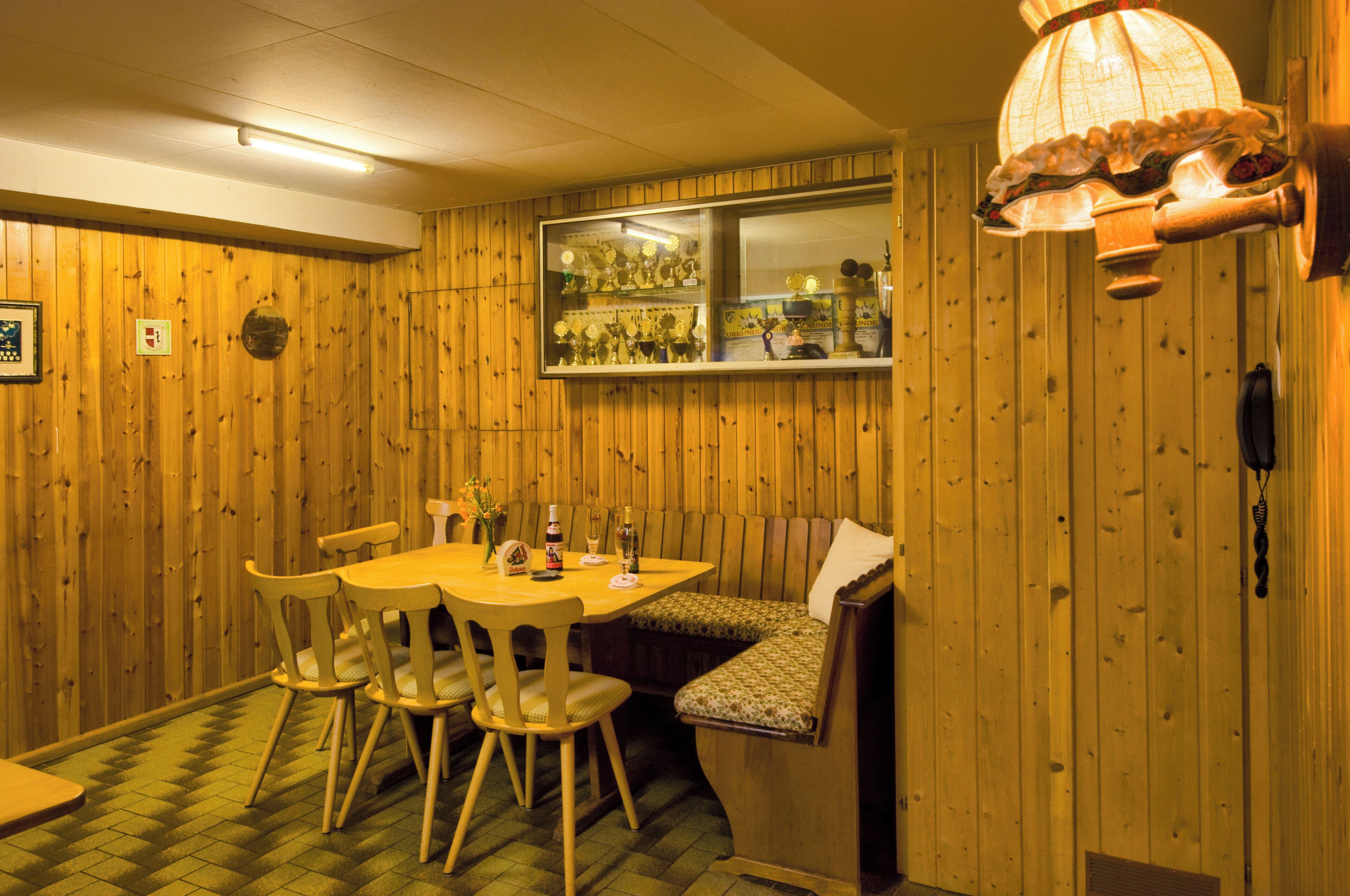 A wooden-paneled room with a dining table, chairs, a bench, and a window displaying trophies.