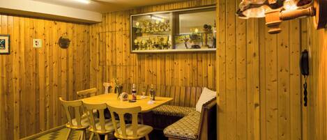 A wooden-paneled room with a dining table, chairs, a bench, and a window displaying trophies.