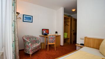 Une chambre d’hôtel avec un lit, un bureau et une chaise, une petite table avec une plante, une armoire et un tableau au mur.