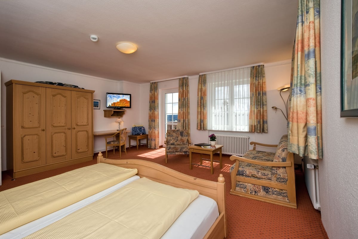 Une chambre d’hôtel avec un lit double, une armoire en bois, une télévision, un bureau avec une chaise, un canapé et une fenêtre avec des rideaux.
