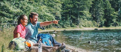 Zwei Personen sitzen am See mit Rucksäcken und einer Trinkflasche.