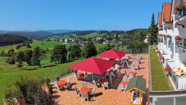 A hotel with outdoor seating and a view of a green valley.