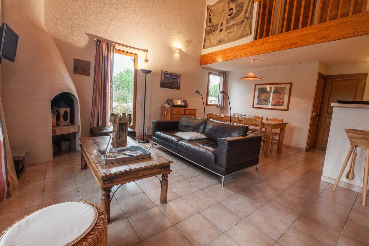A cozy living room with a fireplace, a sofa, a dining table, and a kitchen area.