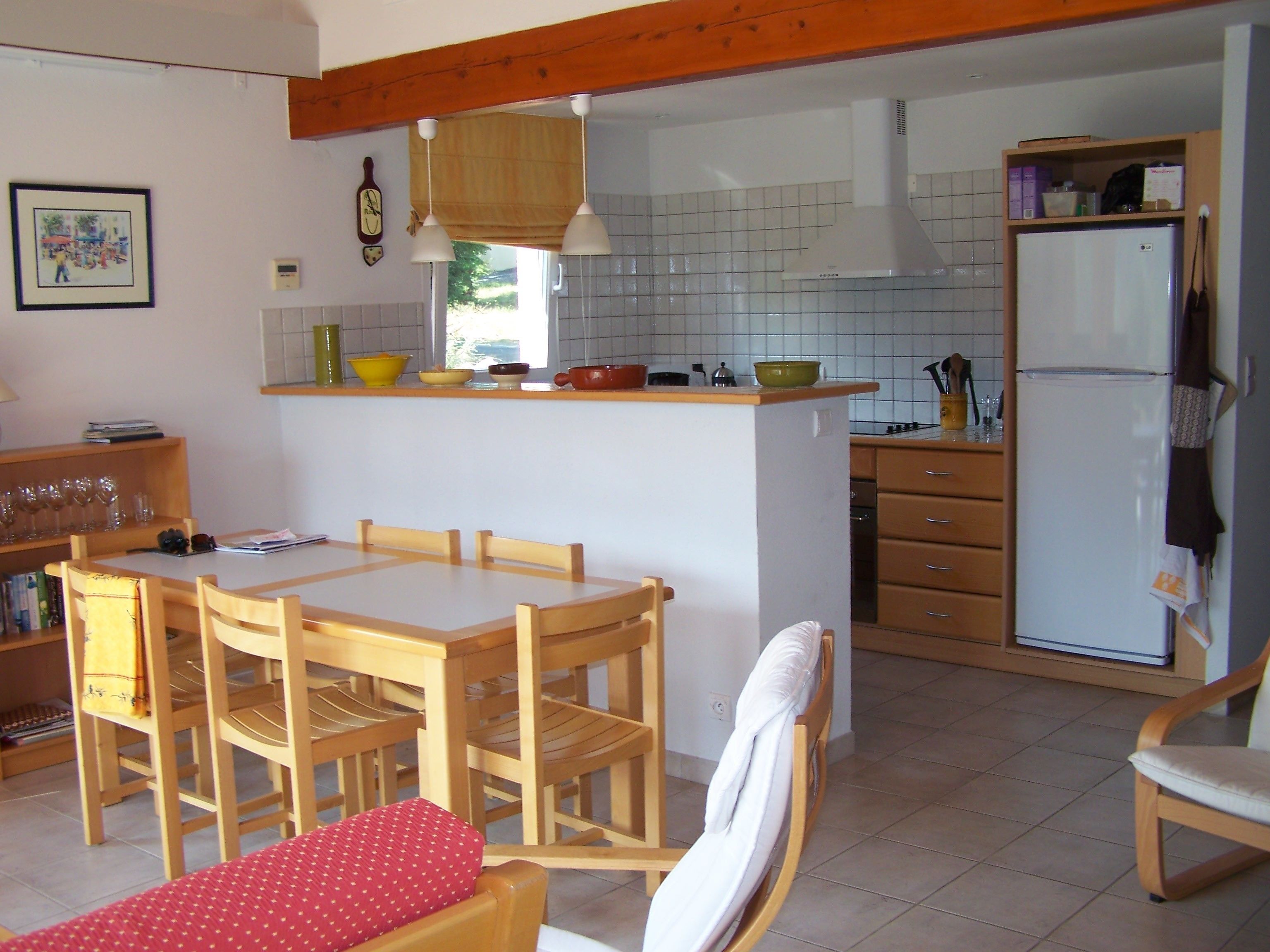 A compact kitchen with a dining area, featuring a wooden table and chairs, a small island with a sink, and a refrigerator.