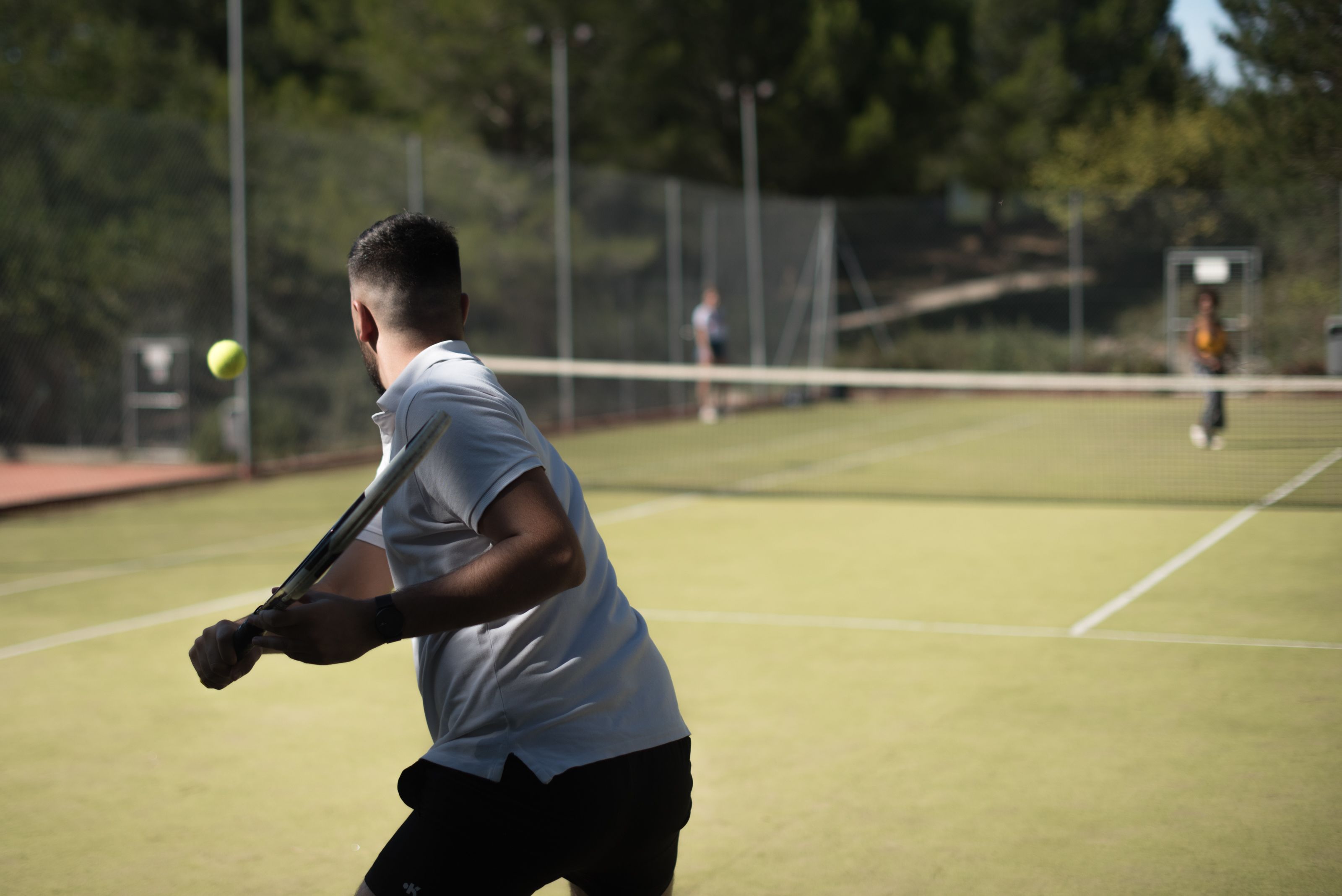Tenniskenttä, jolla valkoista paitaa ja mustia shortseja käyttävä pelaaja valmistautuu lyömään tennispalloa.