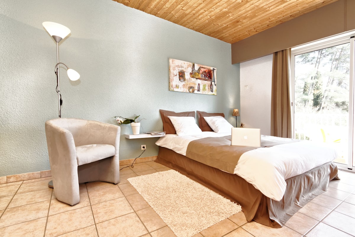 A bedroom with a bed, bedside table, lamp, chair, and a large window.