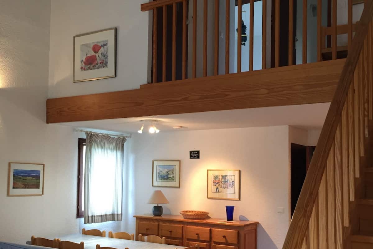 A spacious living area with a dining table, chairs, a sofa, and a staircase.