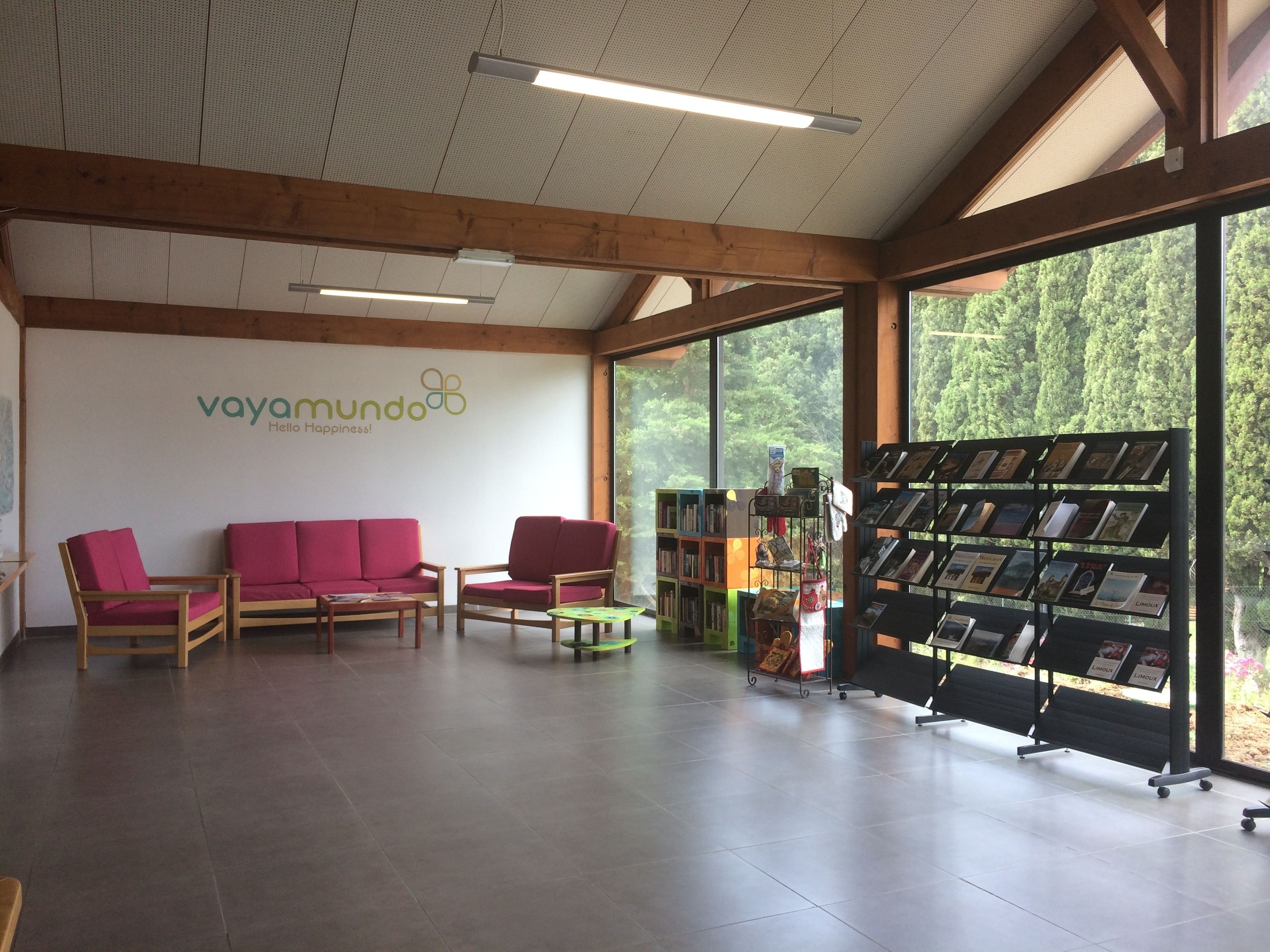A spacious room with a wooden ceiling, a large window, a reception desk, and a bookshelf with books.