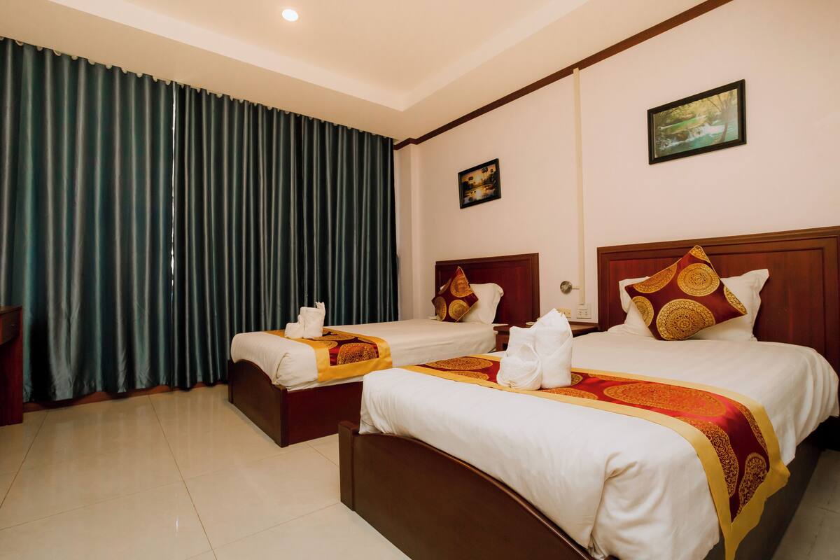 A hotel room with two beds, a large window with curtains, a painting on the wall, and a wooden headboard.