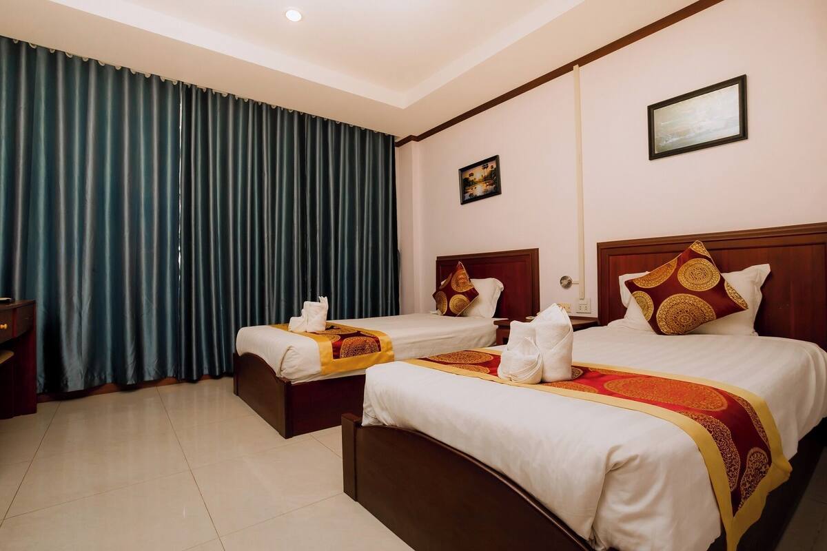 A hotel room with two beds, a large window with curtains, a painting on the wall, and a wooden nightstand.