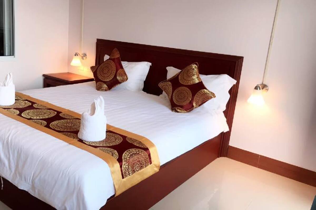 A neatly made bed with a patterned bedspread, pillows with a circular design, and a towel on the bed.