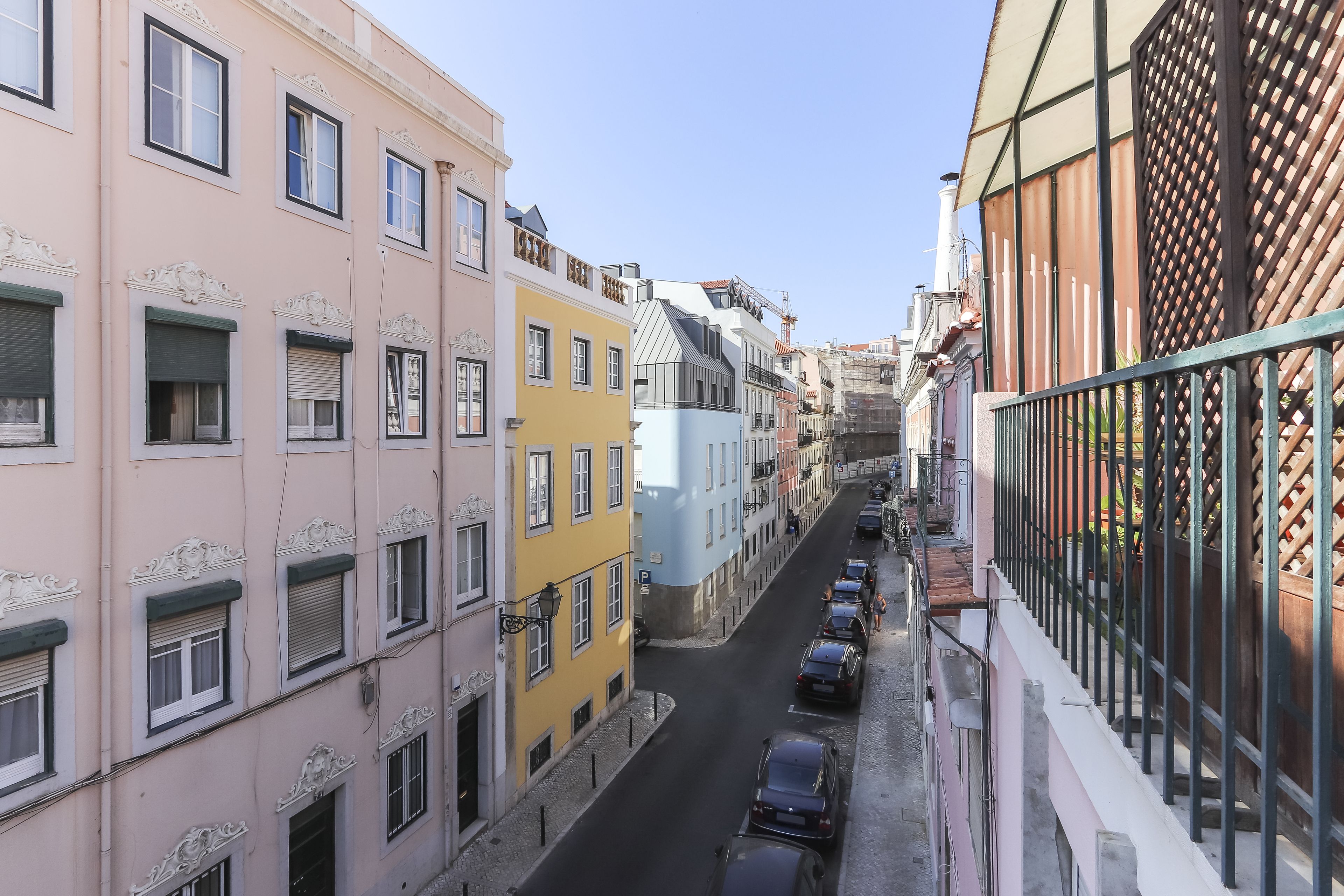 Une rue étroite bordée de bâtiments aux couleurs vives, un ciel dégagé et des voitures garées.