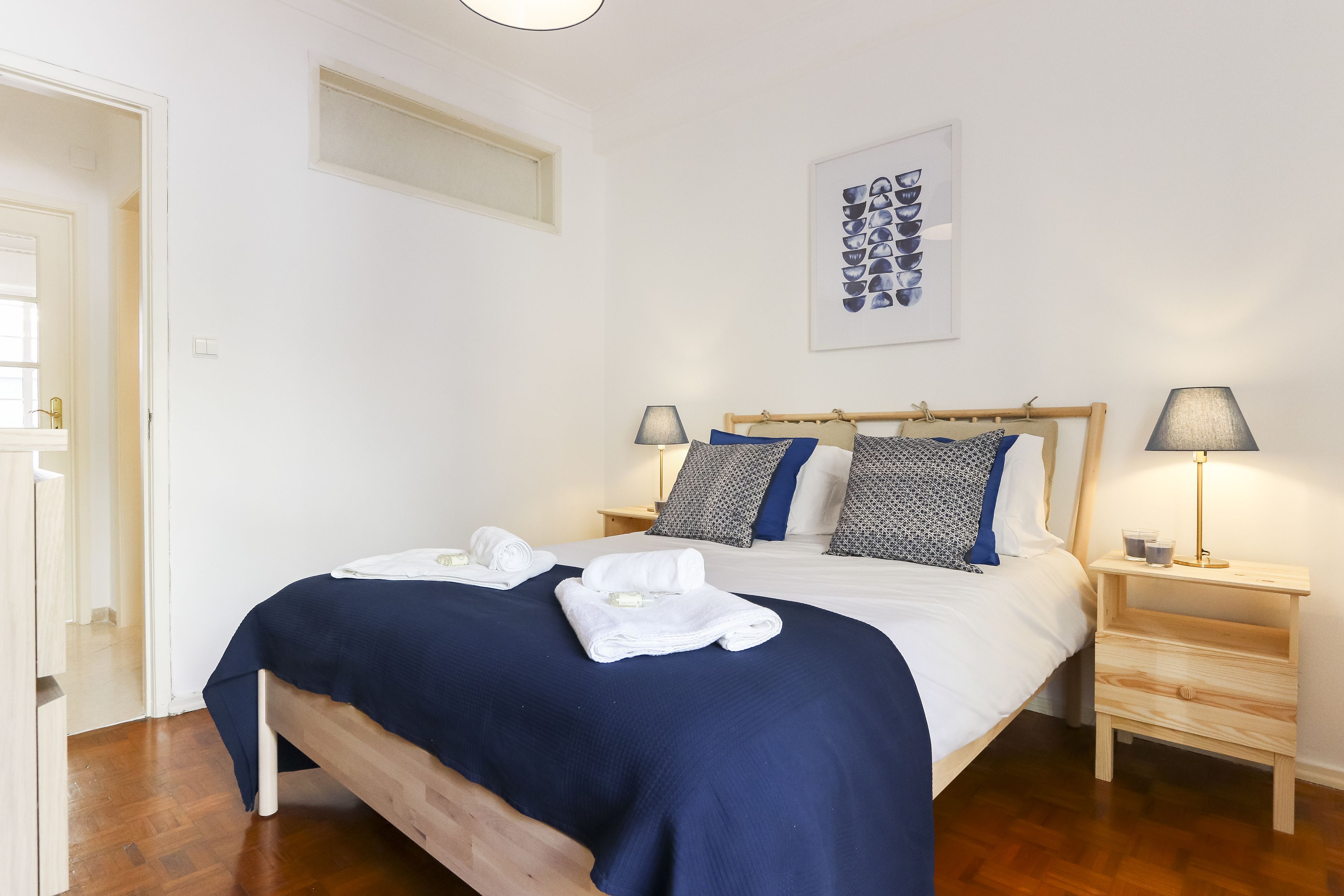 A neatly made bed with a blue bedspread, two bedside lamps, and a wooden nightstand.