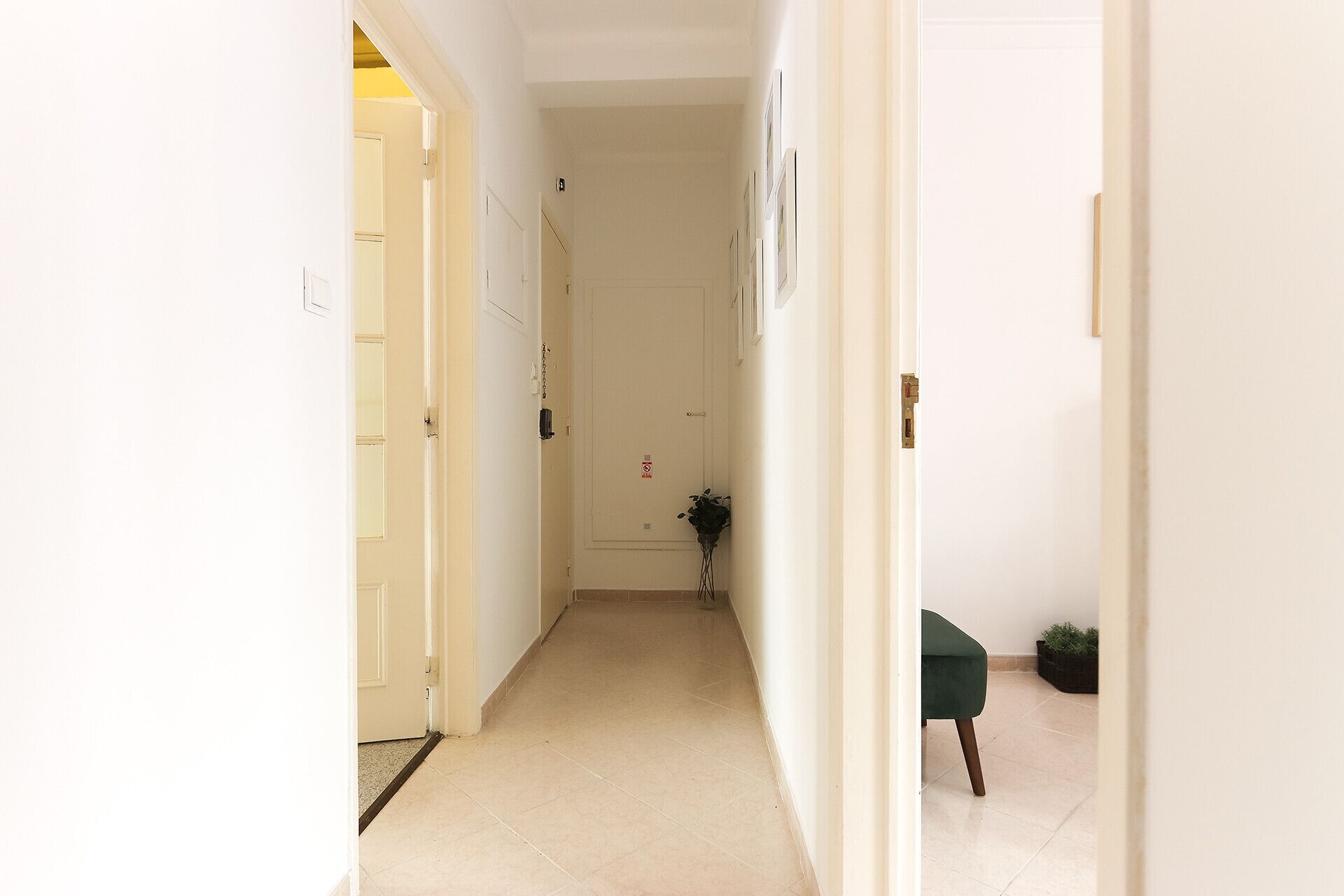 A narrow hallway with white walls and a tiled floor, leading to a door at the end.