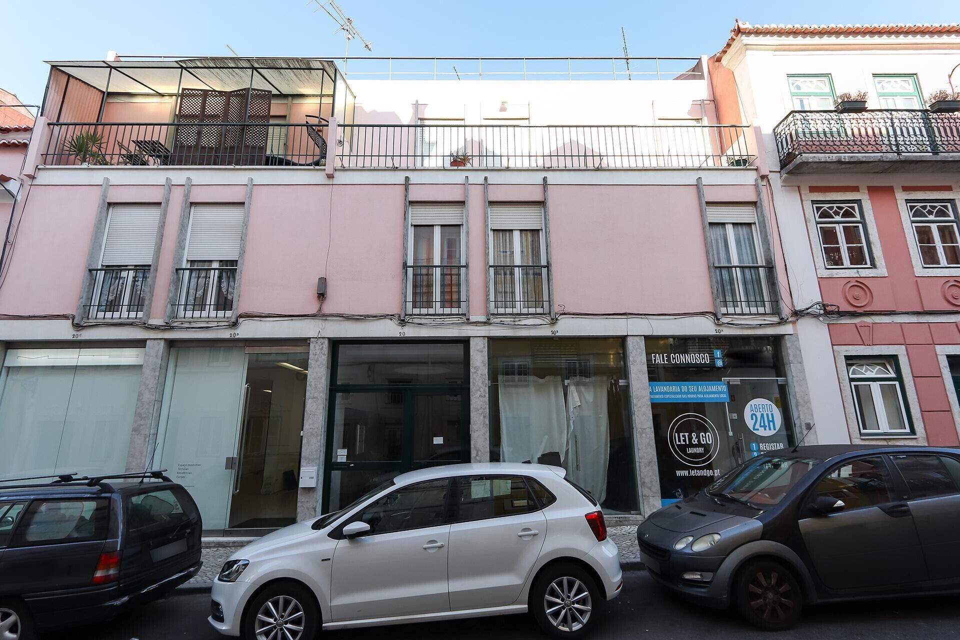 A building with a ground-floor laundry service, a car parked in front, and a balcony with a metal railing.