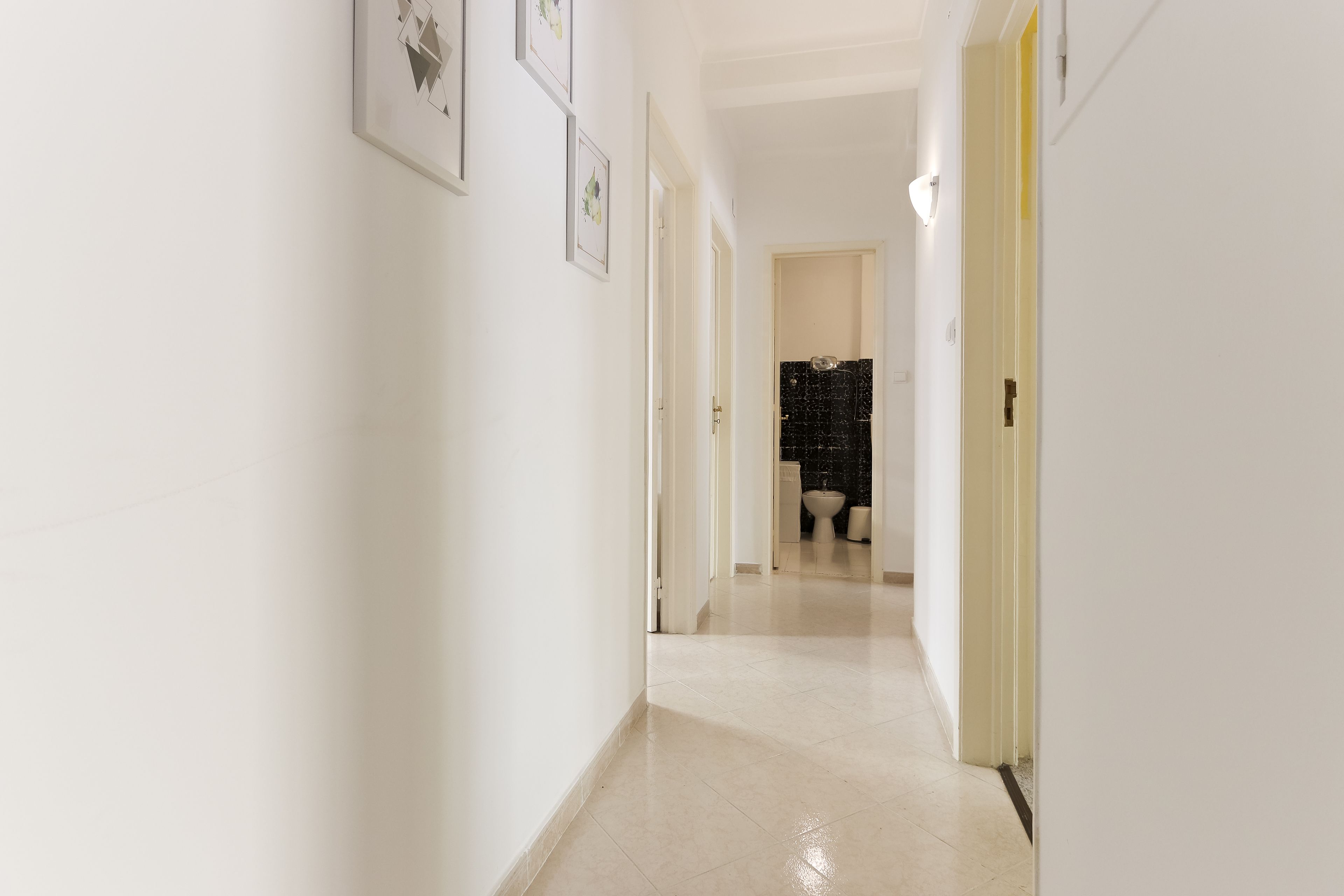 Un pasillo con paredes blancas y piso de baldosas que conduce a una habitación con un muro de baldosas blanco y negro.