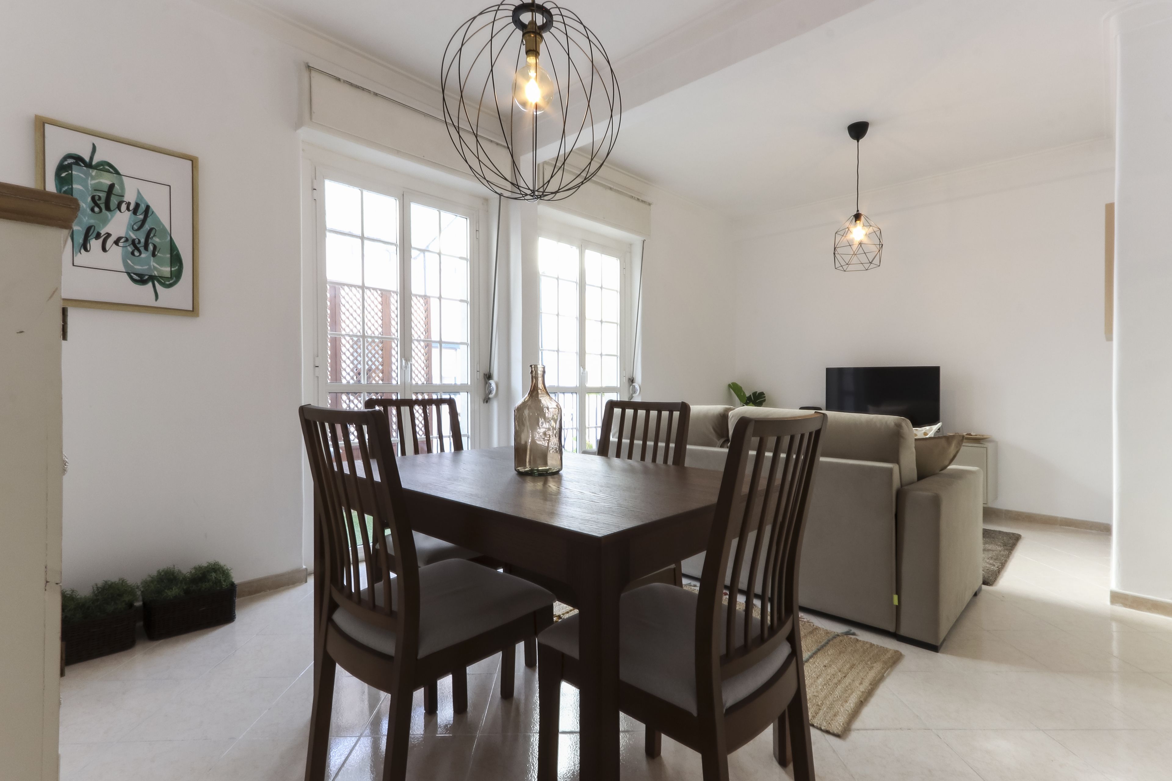 Un comedor con una mesa y sillas de madera, una araña y un sofá al fondo.
