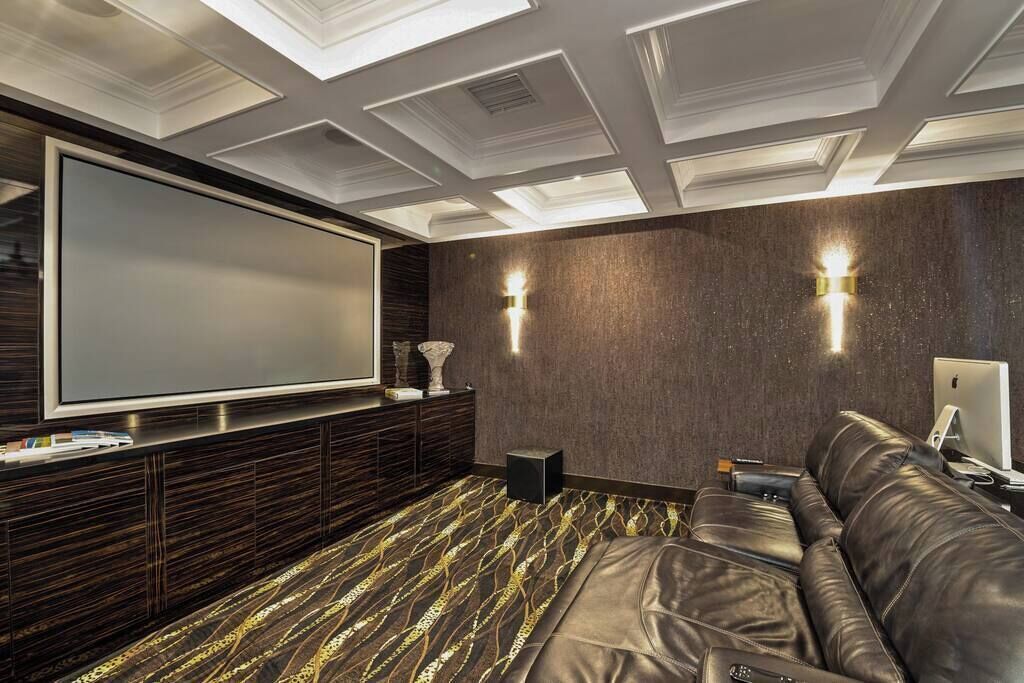 Un salon moderne doté d’un grand téléviseur à écran plat, de lambris en bois foncé, d’un tapis à motifs et d’un canapé en cuir.