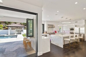 A modern kitchen with a marble island, white cabinetry, and stainless steel appliances. - Stunning Desert Oasis (Palm Desert)