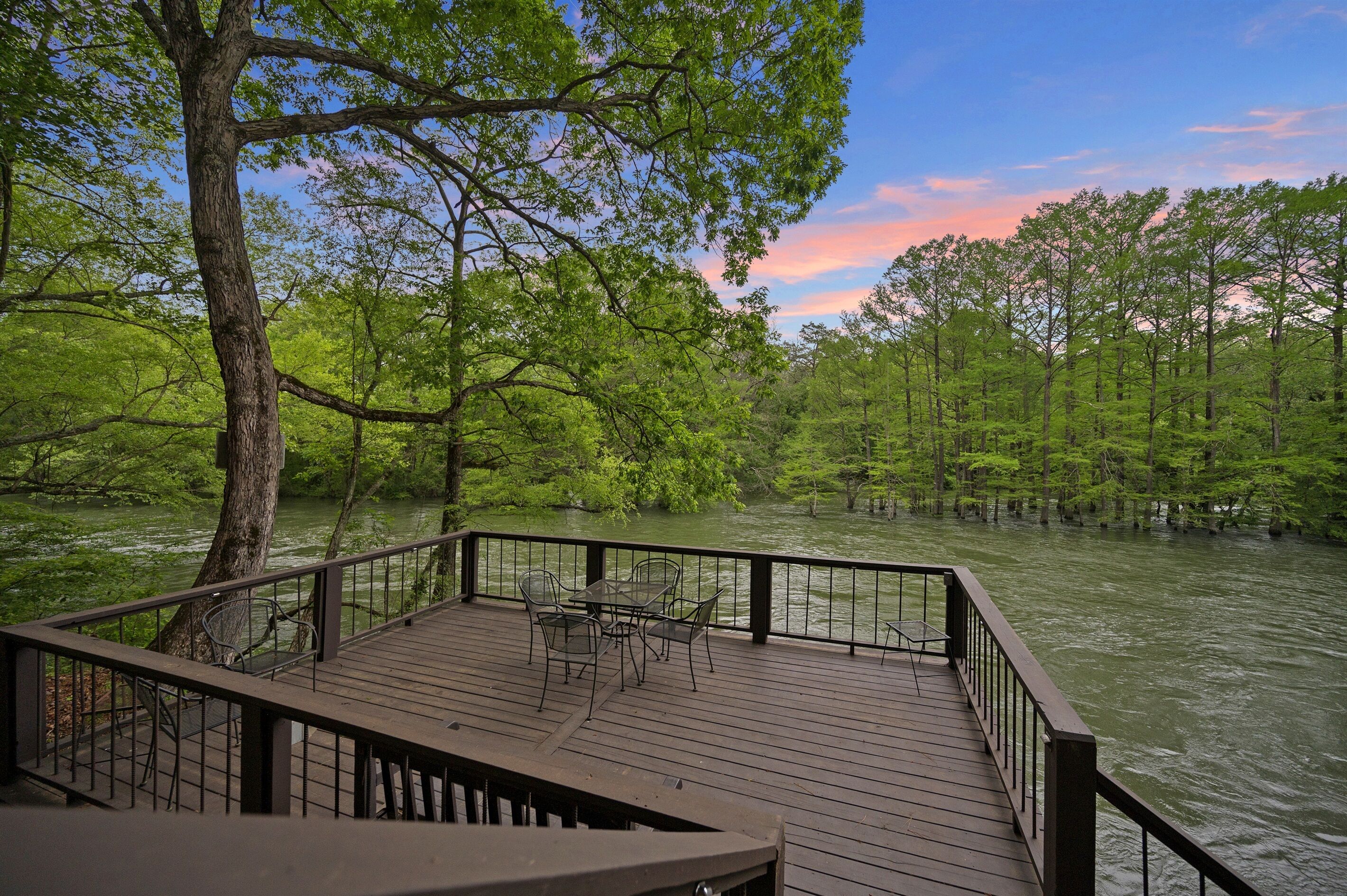 A wooden deck with chairs overlooking a river surrounded by trees.