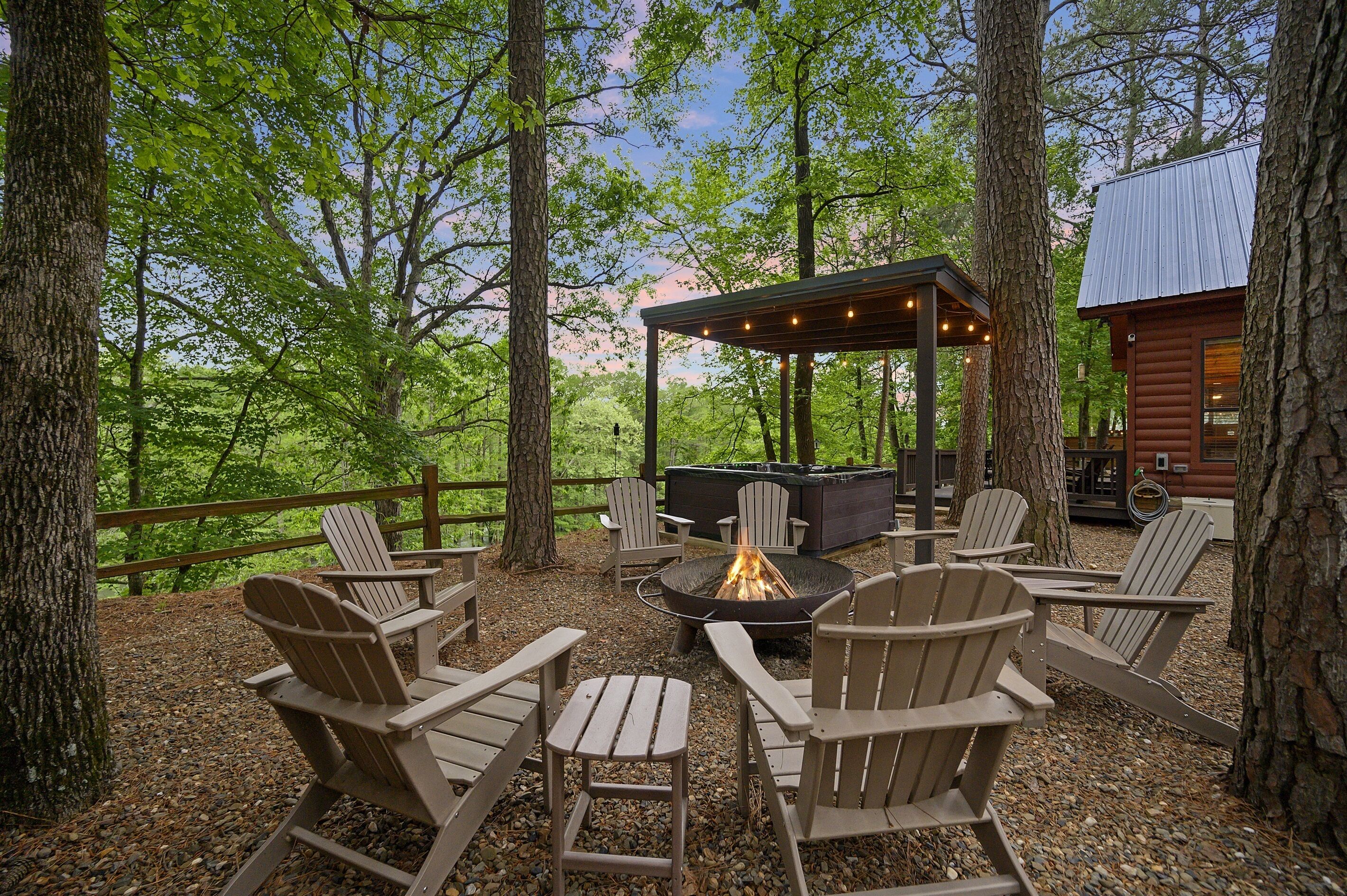 A wooden deck with Adirondack chairs, a fire pit, and a covered seating area surrounded by trees.