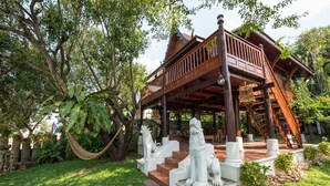 A wooden pavilion with a balcony, surrounded by lush greenery and stone statues. - Phuttal Residence (Ayutthaya)