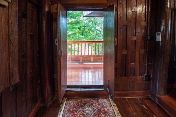 A wooden interior with a view of a wooden deck and lush greenery outside. - Phuttal Residence (Ayutthaya)