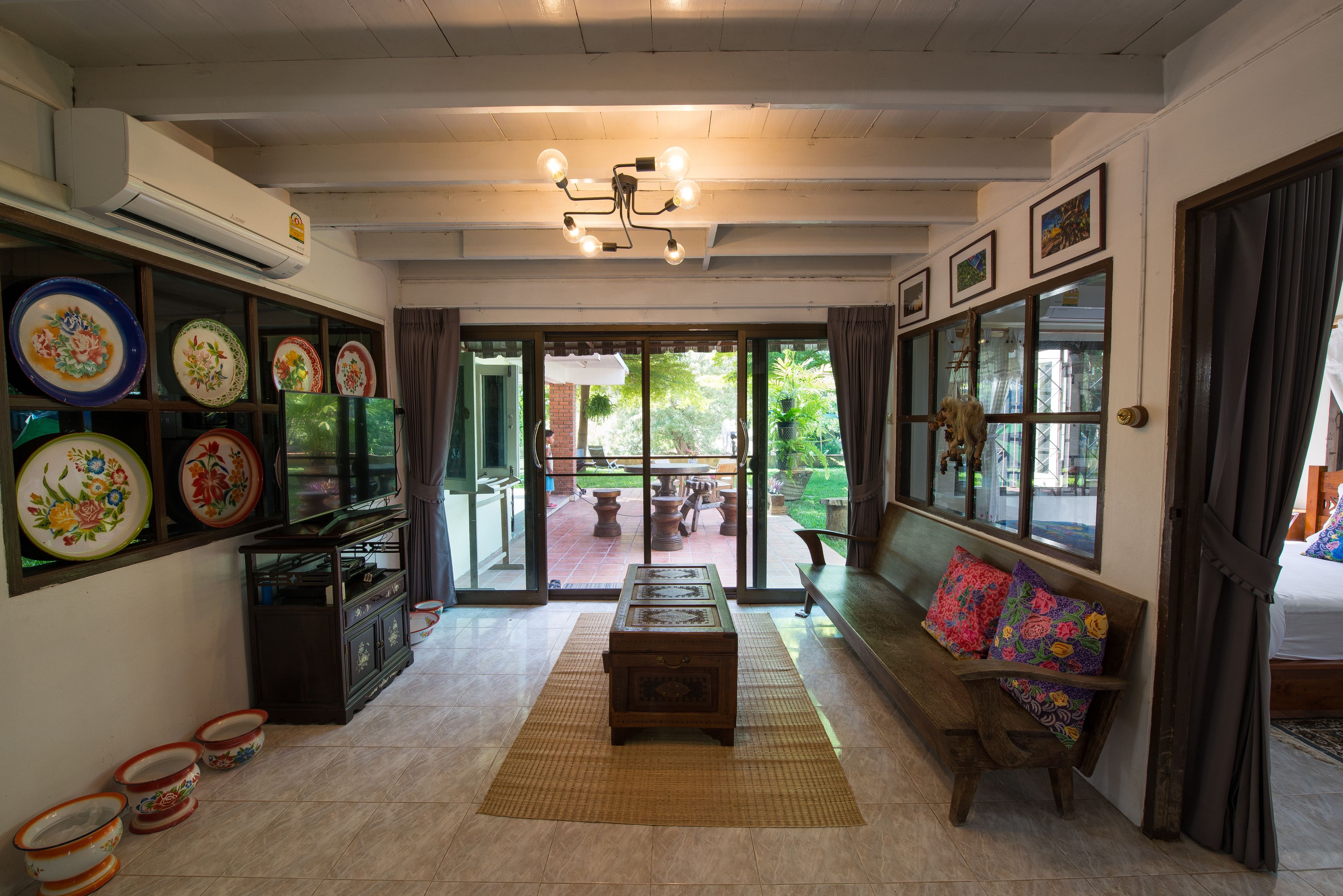 A spacious living room with a wooden bench, a television, and a dining area with colorful plates.